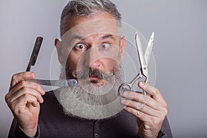 Portrait of mature bearded man with retro razor and scissors, barbershop concept, selective focus