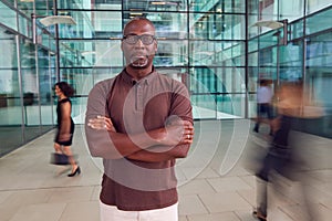 Portrait Of Mature Businessman With Crossed Arms Standing In Lobby Of Busy Modern Office