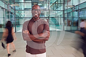 Portrait Of Mature Businessman With Crossed Arms Standing In Lobby Of Busy Modern Office