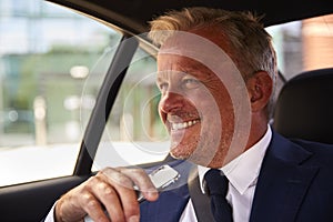 Portrait Of Mature Businessman Holding Mobile Phone In Back Of Taxi Or Car