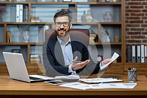 Portrait of mature businessman inside office at workplace, man with documents smiling and looking at camera, paperwork