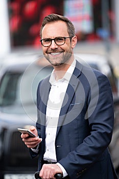 Portrait Of Mature Businessman With Mobile Standing By Taxi Rank Outside Railway Station