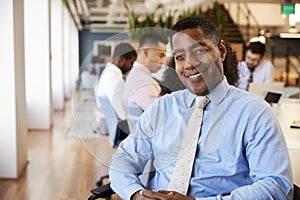 Portrait Of Mature Businessman In Modern Office With Colleagues Meeting Around Table In Background