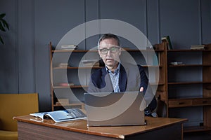 Portrait of mature businessman in suit pensivly working on the laptop in his office