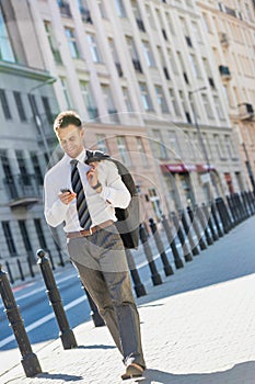 Portrait of mature businessman using smartphone while walking on pavement after work