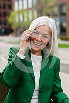 Portrait of mature businesswoman making phone call on smartphone, going home from work. Beautiful older woman with gray