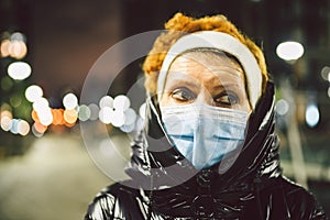 Portrait mature Caucasian woman in protective medical mask on face against background of evening city in winter. An elderly woman