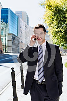 Portrait of mature confident businessman smiling and talking on smartphone while walking on pavement