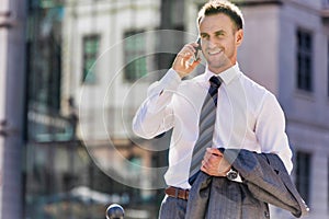 Portrait of mature confident businessman smiling and talking on smartphone while walking on pavement