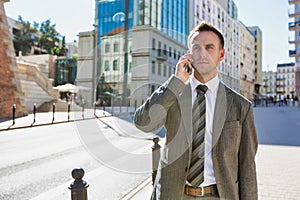 Portrait of mature confident businessman smiling and talking on smartphone while walking on pavement