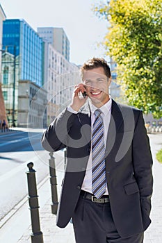 Portrait of mature confident businessman smiling and talking on smartphone while walking on pavement