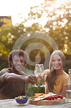 Portrait Of Mature Couple Celebrating With Champagne As They Sit At Table In Garden With Snacks