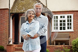 Portrait Of Mature Couple Standing In Garden In Front Of Dream Home In Countryside