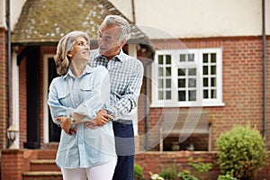 Portrait Of Mature Couple Standing In Garden In Front Of Dream Home In Countryside