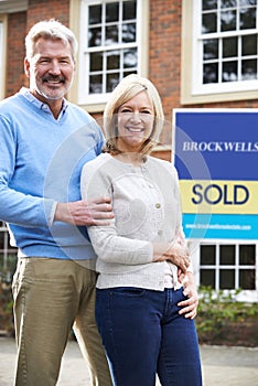 Portrait Of Mature Couple Standing Outside Dream Home Wit Sold Sign