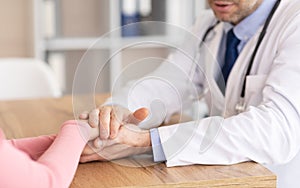 Portrait of mature doctor holding female patient`s hands