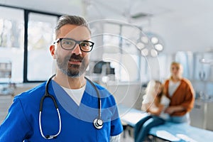 Portrait of mature doctor in surgery room, mother with child in background.