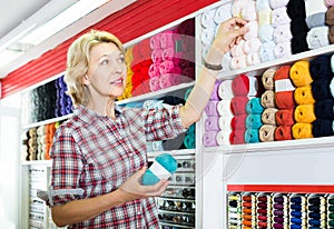 Portrait of mature female customer standing next to shelf with knitting yarn in shop
