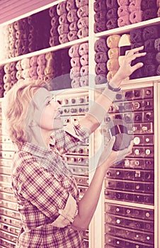 portrait of mature female customer standing next to shelf with knitting yarn in shop