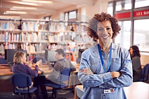 Portrait Of Mature Female Teacher Or Student In Library With Other Students Studying In Background