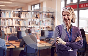 Portrait Of Mature Female Teacher Or Student In Library With Other Students Studying In Background