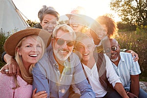 Portrait Of Mature Friends By Tent On Camping Vacation Against Setting Sun