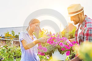 Portrait of mature gardener showing woman buyer flowers on pot in shop
