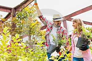 Portrait of mature gardeners smiling while talking and holding flower pot