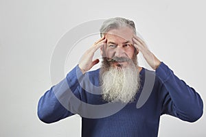 Portrait of mature gray-haired bearded man in blue sweatshirt with a headache on gray background, selective focus