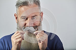 Portrait of mature gray-haired bearded man in blue sweatshirt with mustache comb on gray background, selective focus