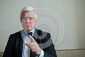 Portrait of a mature gray-haired serious man in a suit and bow-tie. An elegantly dressed, clean-shaven senior looks