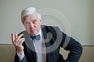 Portrait of a mature gray-haired serious man in a suit and bow-tie. An elegantly dressed, clean-shaven senior looks