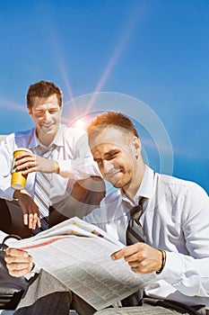 Portrait of mature handsome businessman reading newspaper against collegue during break