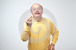 Portrait of mature handsome man in yellow shirt showing italian gesture that means what do you want