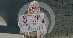 Portrait of mature lady raising Stop Racism sign protesting against racial inequality standing in city on sunny day