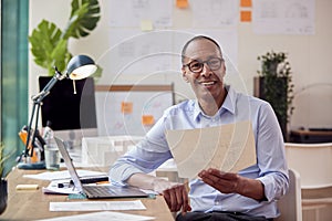 Portrait Of Mature Male Architect Working In Office At Desk Studying Plans For New Building