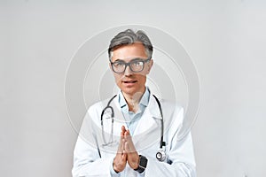 Portrait of mature male doctor or physician in white coat with stethoscope around neck praying to God for help while