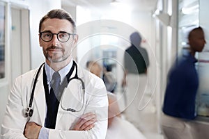 Portrait Of Mature Male Doctor Wearing White Coat With Stethoscope In Busy Hospital Corridor photo