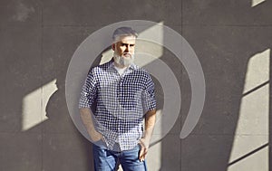 Portrait of mature male model in casual shirt and jeans standing by grey studio wall
