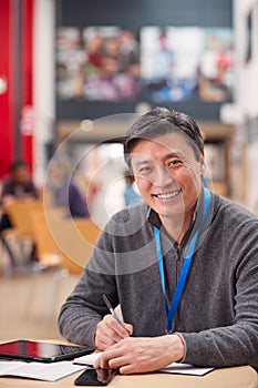 Portrait Of Mature Male Teacher Or Student With Digital Tablet Working At Table In College Hall