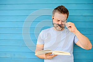 Portrait of mature man with big black eye glasses trying to read book but having difficulties seeing text because of vision