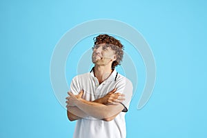 Portrait of mature man with curly hair in white t-shirt standing with dreaming face against blue studio background