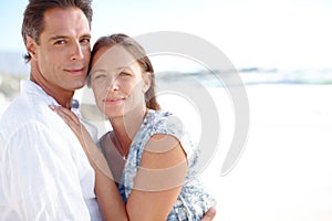 Portrait of a mature man embracing his happy wife from behind as they stand on the beach