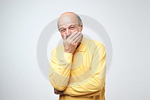 Portrait of mature man laughing and covering his mouth with hand over white background.