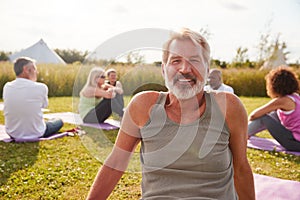 Portrait Of Mature Man On Outdoor Yoga Retreat With Friends And Campsite In Background photo