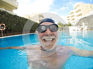 Portrait of mature man smiling and looking at the camera in the pool having fun alone - training and swimming happy - close up of