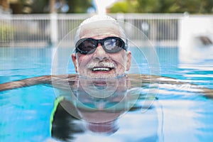 Portrait of mature man smiling and looking at the camera in the pool having fun alone - training and swimming happy - close up of