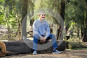 portrait mature man spend leisure time sitting on a log in the forest park