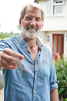 Portrait Of Mature Man Standing In Garden In Front Of Dream Home In Countryside Holding Keys