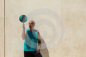 portrait of mature man on street basketball court against a wall playing with a ball